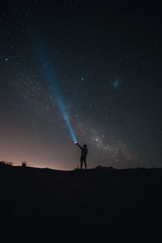 a person standing on top of a hill under a night sky, a microscopic photo, pexels contest winner, light and space, holding a light saber, andromeda, standing in the solar system, small people with torches