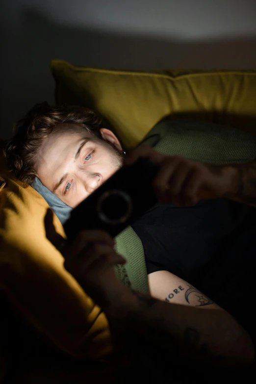 a man laying in bed holding a camera, a portrait, inspired by Elsa Bleda, trending on pexels, renaissance, lil peep, night mood, pete davidson, playing video games