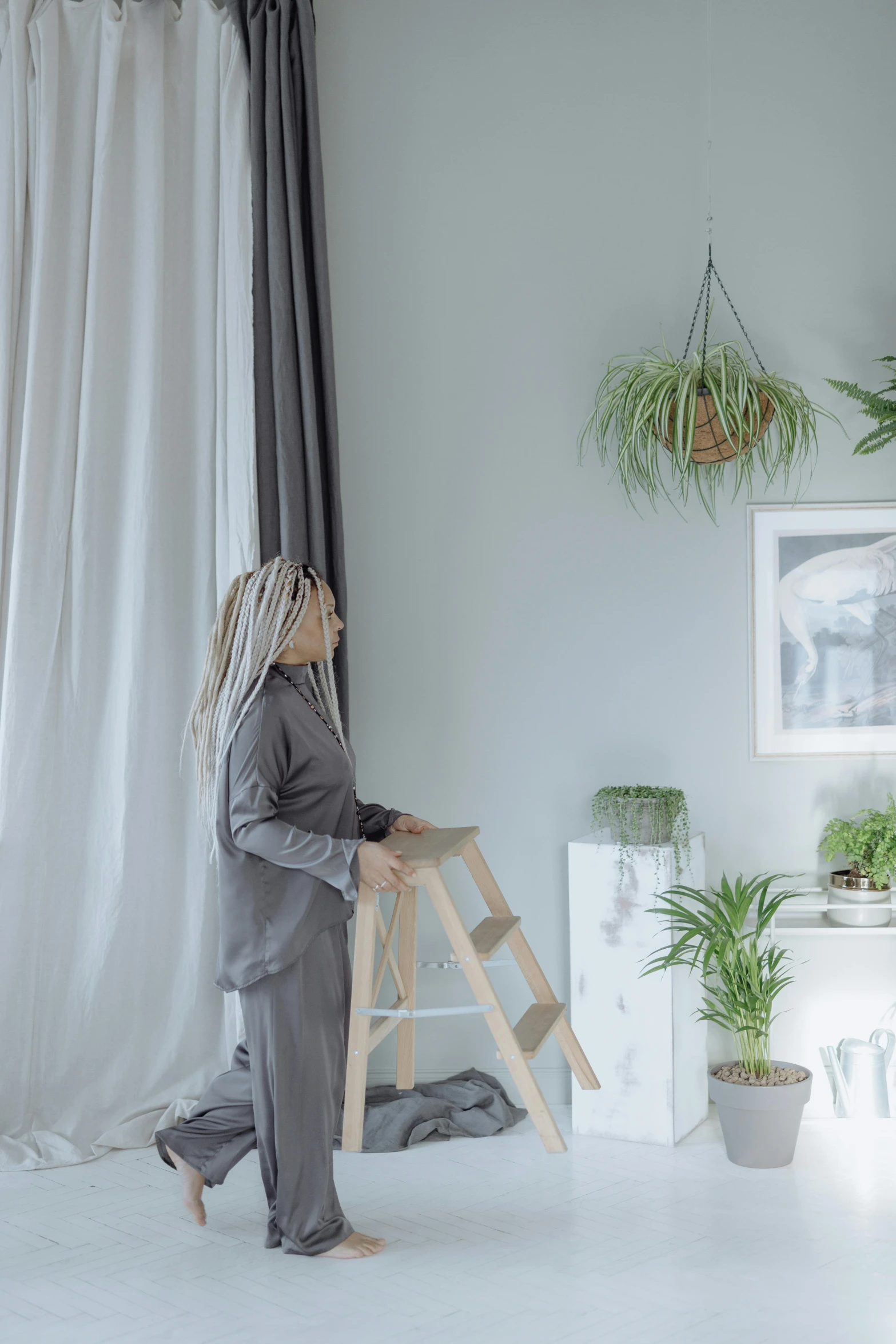 a woman standing next to a ladder in a room, trending on unsplash, curtains, houseplant, grey colours, low quality photo