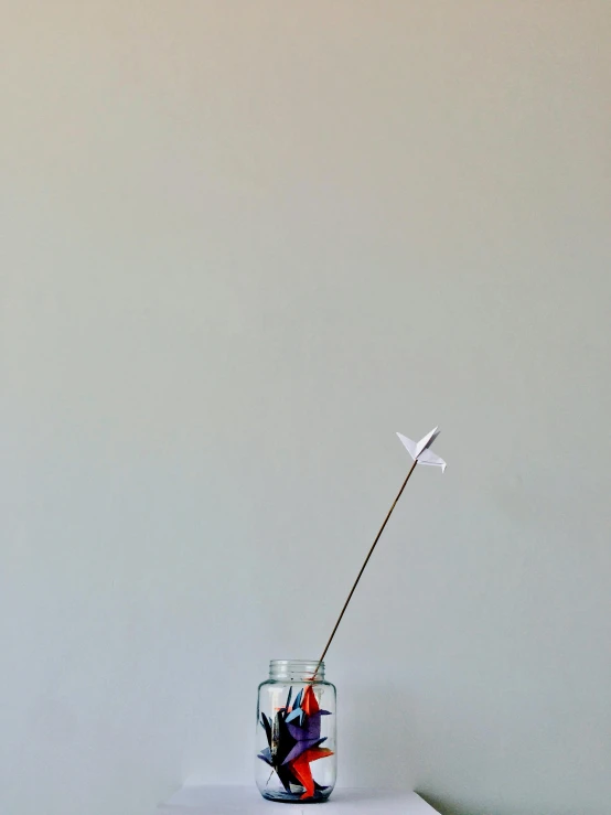 a vase sitting on top of a white table, a minimalist painting, inspired by Alexander Calder, unsplash, kinetic art, cessna glider plane, firework, glass jar, 9 0 mm studio photograph tiny