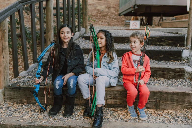 three children sitting on steps with bows and arrows, pexels contest winner, adventure playground, avatar image, hunting, cast