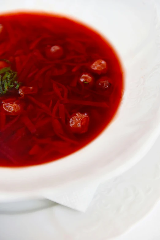 a bowl of soup sitting on top of a white plate, inspired by Géza Dósa, pexels, renaissance, in crimson red, jelly - like texture, threads, mint