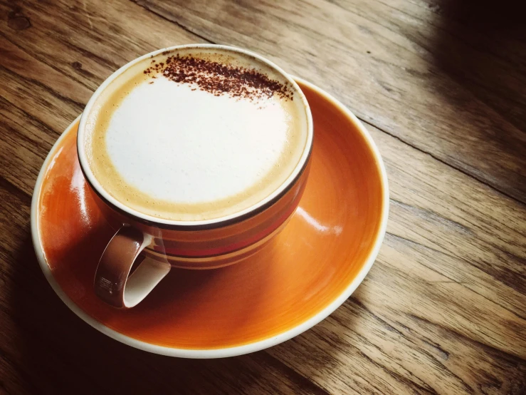 a close up of a cup of coffee on a saucer, a photo, unsplash, sitting on a mocha-colored table, orange and white color scheme, “ iron bark, no cropping