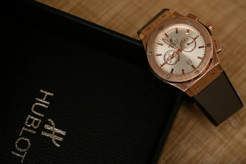 a watch sitting on top of a black book, hurufiyya, hublot, ivory and copper, thumbnail, close up image