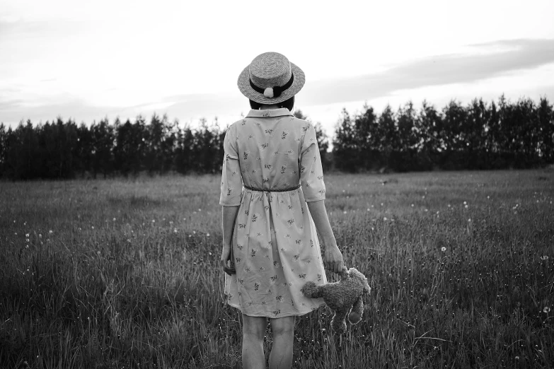 a woman standing in a field holding a teddy bear, a black and white photo, by Lucia Peka, pexels, woman with hat, wearing in a summer dress, loneliness, 15081959 21121991 01012000 4k