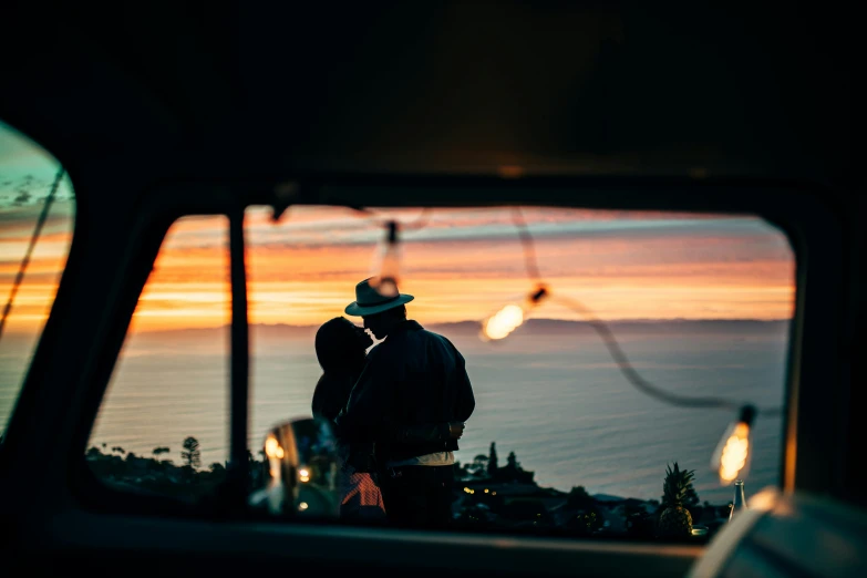 a man that is standing in the back of a truck, by Lee Loughridge, unsplash contest winner, romanticism, ocean cliff view, couple kissing, kombi, bright lights