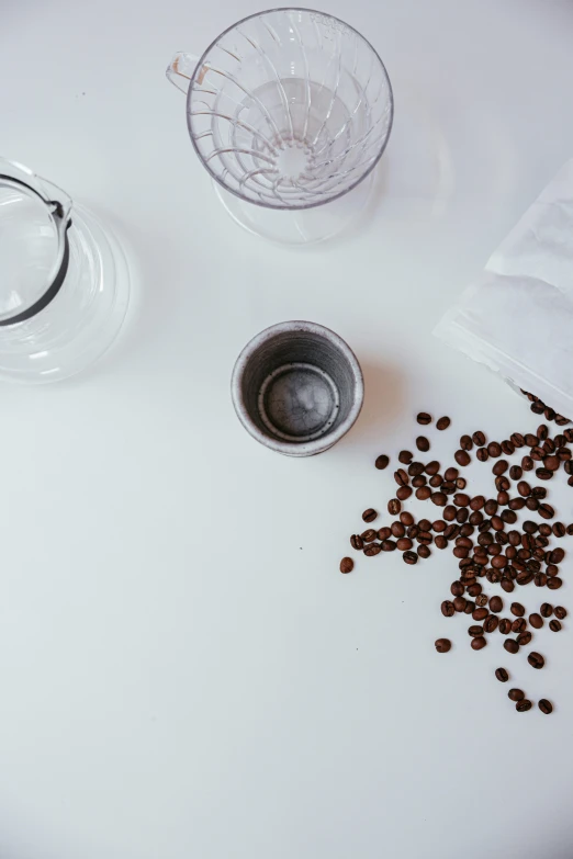 a white table topped with coffee beans and a cup, beakers, product view, medium-shot, detail shot