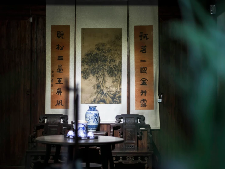 a table and chairs in a room with a painting on the wall, inspired by Zhang Shunzi, trending on unsplash, tea drinking and paper lanterns, ancient library, phuoc quan, portait photo