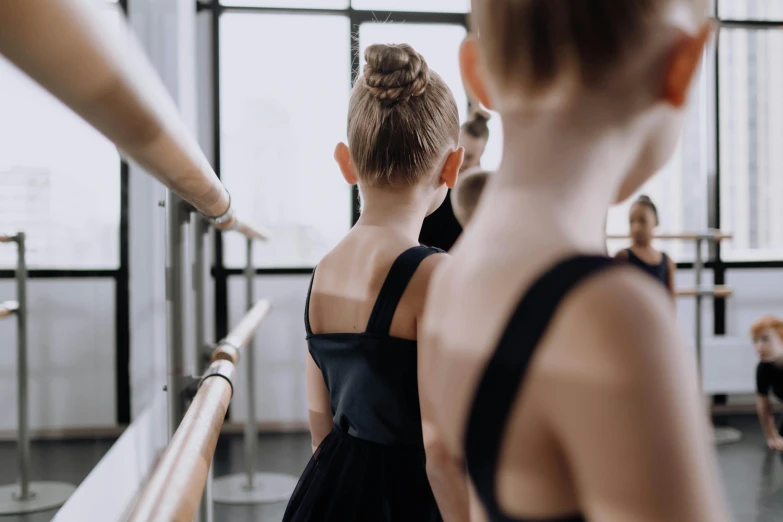 a group of young girls standing next to each other in a dance studio, by Emma Andijewska, pexels contest winner, arabesque, showing her shoulder from back, zoomed in, blank, looking serious