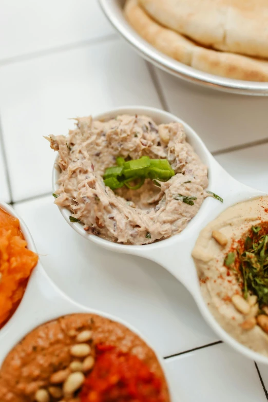 a table topped with bowls of food next to pita bread, humus, ivy's, medium close shot, 6 pack