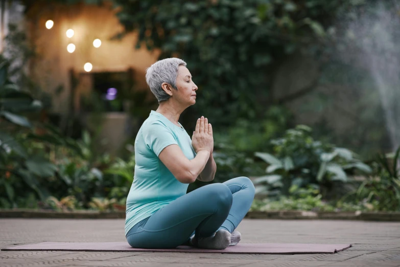 a woman sitting in the middle of a yoga pose, profile image, an elderly, lush surroundings, health supporter