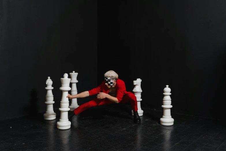 a man in a red suit is surrounded by white chess pieces, by Emma Andijewska, pexels contest winner, video art, playful pose of a dancer, masked person in corner, crawling out of a dark room, quicksilver