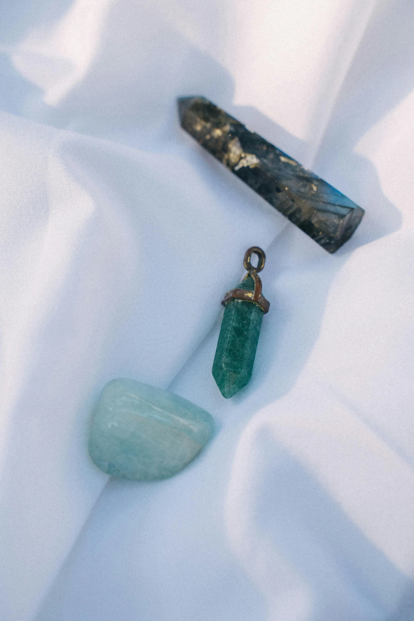 a couple of green stones sitting on top of a white sheet, by Jessie Algie, unsplash, pendants, blue crystals, weathered artifacts, healing tubes