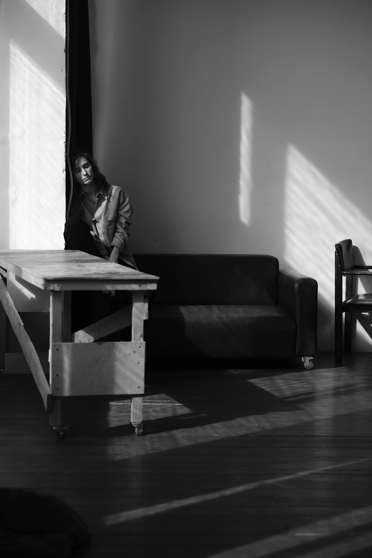 a black and white photo of a person sitting at a table, with furniture overturned, studio backlight, julia sarda, a wooden