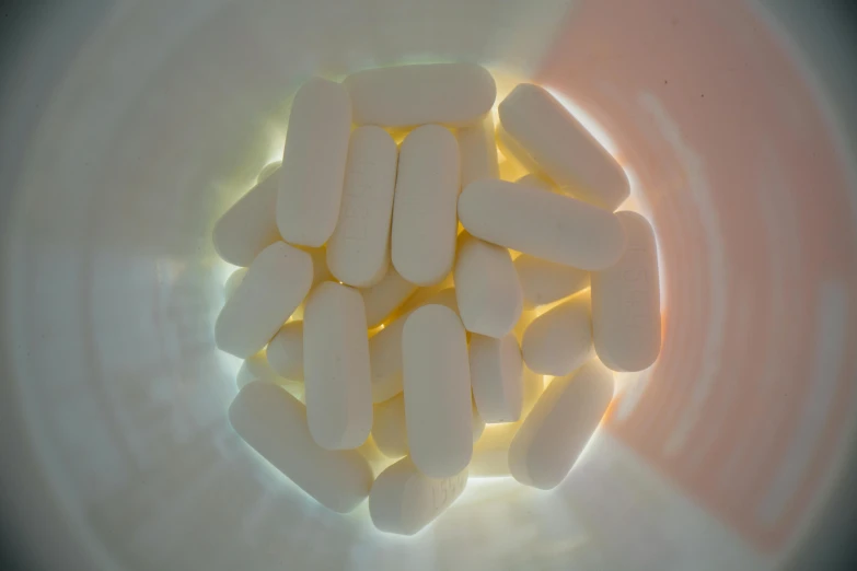 a bowl filled with white pills sitting on top of a table, soft coloured gel lighting, view from bottom to top, with glow on some of its parts, vanilla