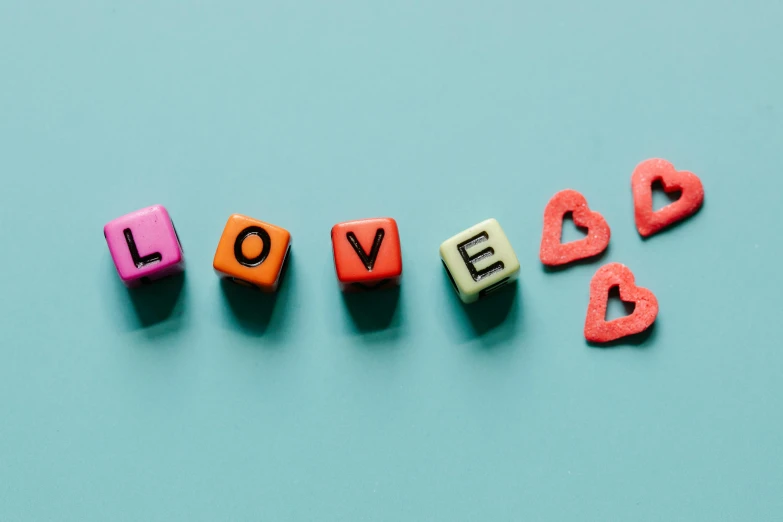 the word love spelled with wooden letters on a blue background, by Sylvia Wishart, trending on pexels, pink and teal and orange, cubes, red hearts, on a canva