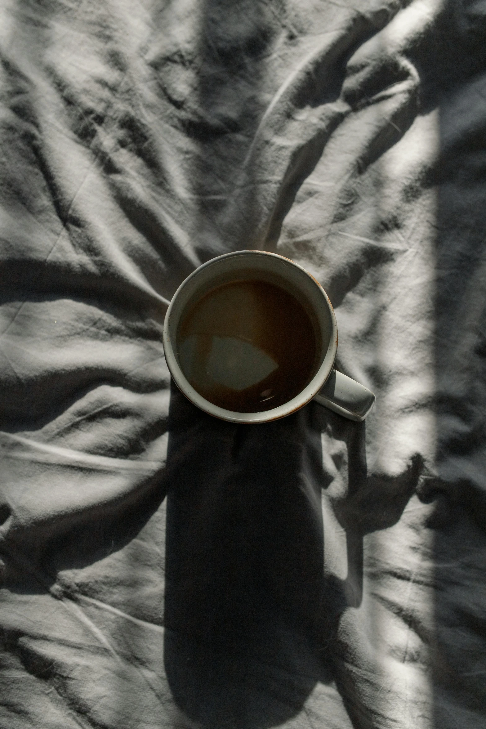 a cup of coffee sitting on top of a bed, inspired by Elsa Bleda, trending on unsplash, photorealism, shadowy, ignant, gray canvas, full sun