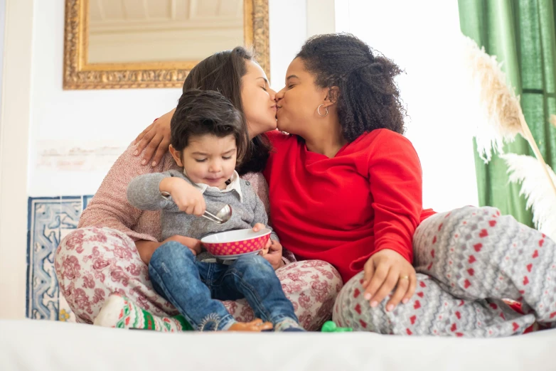 a woman and two children sitting on a bed, pexels, lesbian kiss, red sweater and gray pants, sitting on a couch, diverse