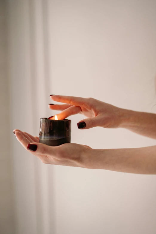 a woman holding a candle in her hand, by Nina Hamnett, light and space, black and terracotta, magical potions, handcrafted, highly polished