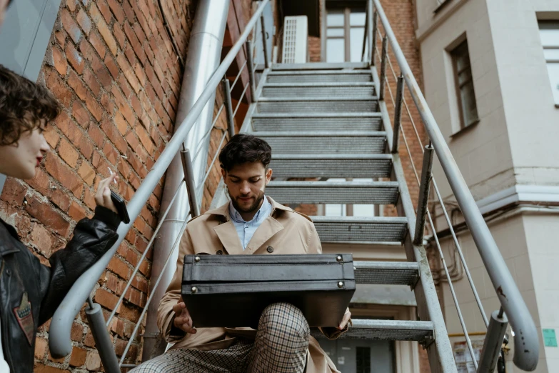 a man sitting on a set of stairs using a laptop, by Adam Marczyński, pexels contest winner, holding a briefcase, musicians, brown, promotional image