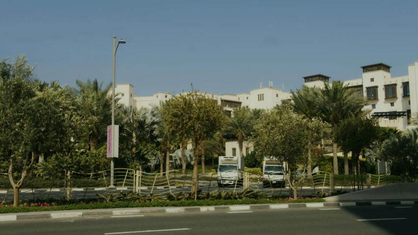 a white truck driving down a street next to tall buildings, hurufiyya, date trees, medical complex, tourist photo, ap