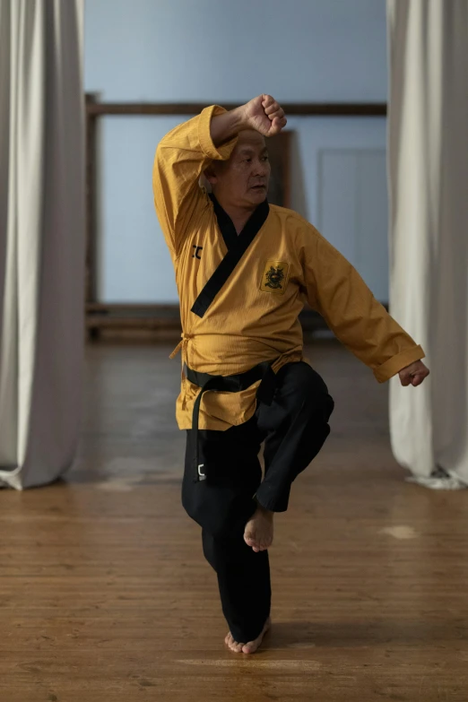 a man standing on one leg in a karate pose, inspired by Ma Quan, unsplash, shin hanga, with yellow cloths, square, 7 0 years old, kim doyoung