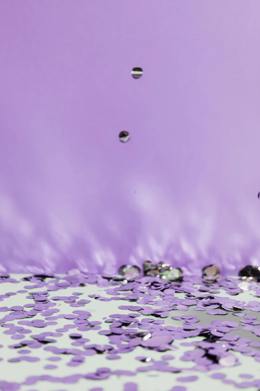 a bunch of confetti sitting on top of a table, inspired by Lucio Fontana, trending on unsplash, conceptual art, purple water, made of liquid metal, pastel purple background, reflection in water