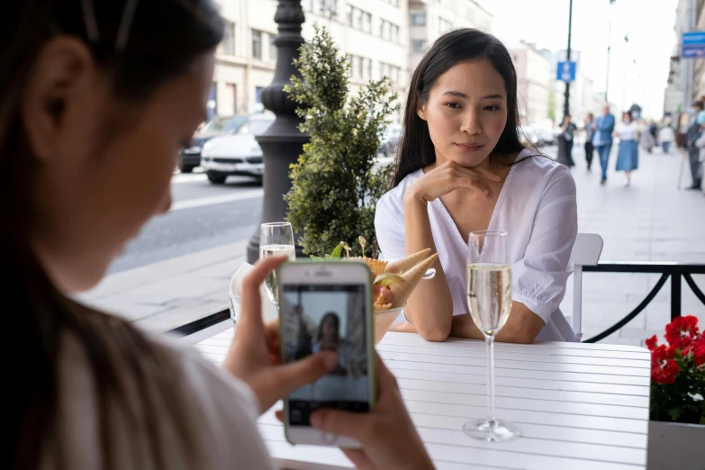 a woman sitting at a table with a glass of wine, pexels contest winner, smartphone footage, two still figures facing camera, asian features, champagne commercial