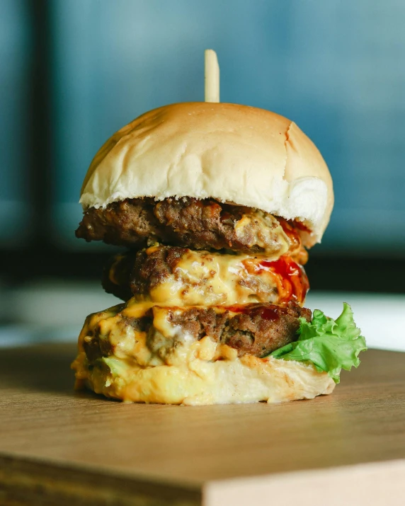 a hamburger sitting on top of a wooden cutting board, by Austin English, unsplash, melted cheddar, malaysian, stacked, thumbnail