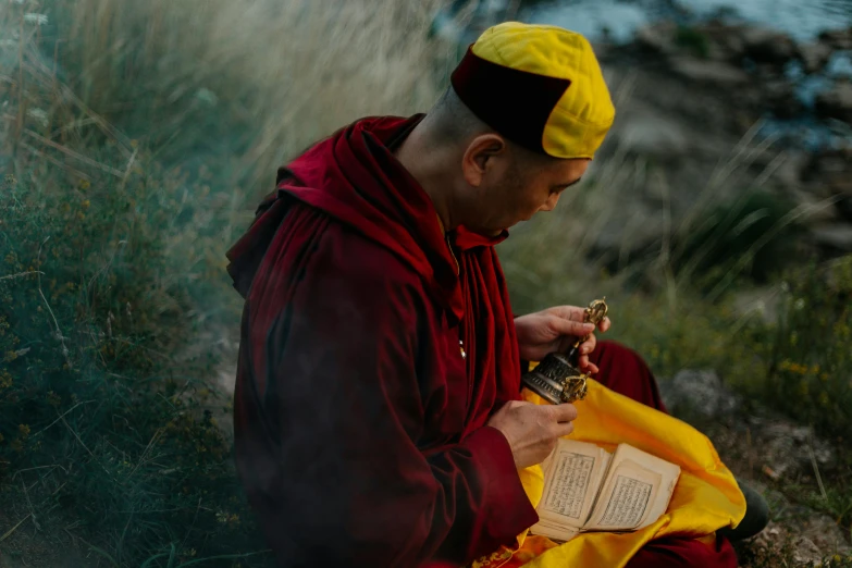 a man sitting on the ground reading a book, a picture, by Matthias Stom, pexels contest winner, taoist robe, red and yellow scheme, holding a bottle, lama