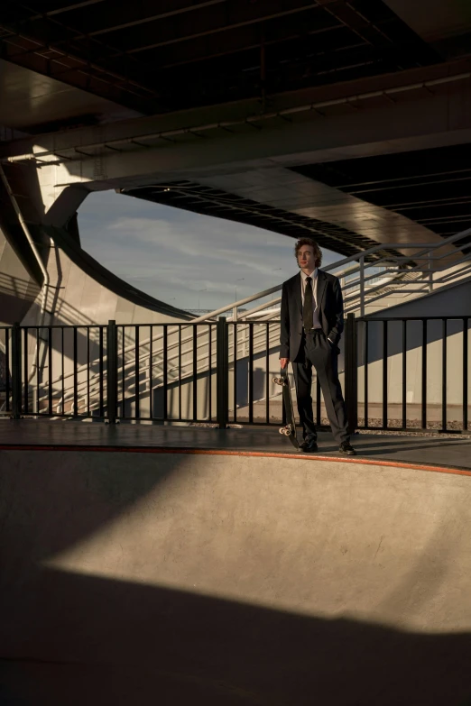 a man in a suit standing on a skateboard ramp, by David Palumbo, overpass, evening light, daniel libeskind, principal set photography