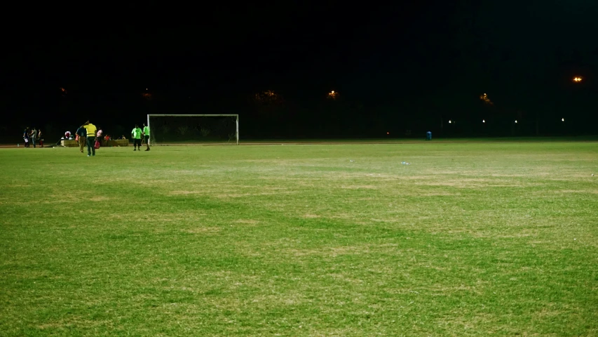 a group of people standing on top of a lush green field, pitch darkness around the post, practice, during night, dark taint :: athletic