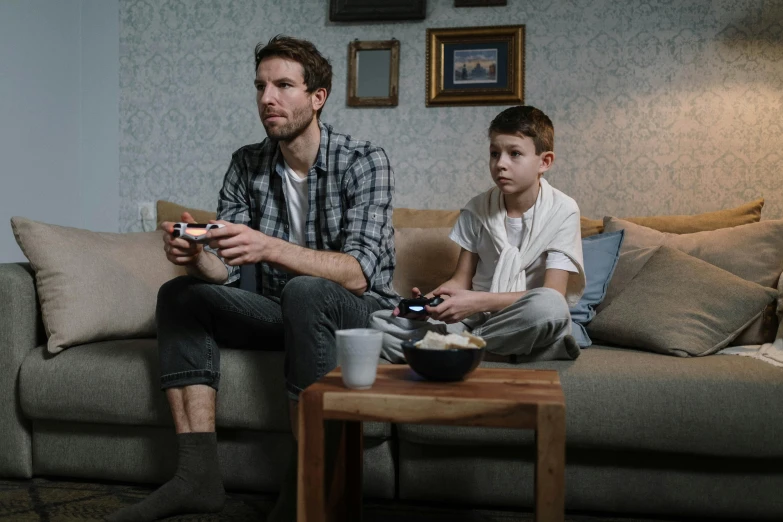 a man and a boy sitting on a couch playing a video game, by Adam Marczyński, pexels, hyperrealism, 15081959 21121991 01012000 4k, looking sad, looking towards camera, ignant