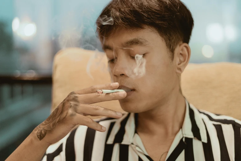 a man sitting in a chair smoking a cigarette, inspired by Gang Hui-an, trending on pexels, left eye stripe, thawan duchanee, male teenager, high cheek bones