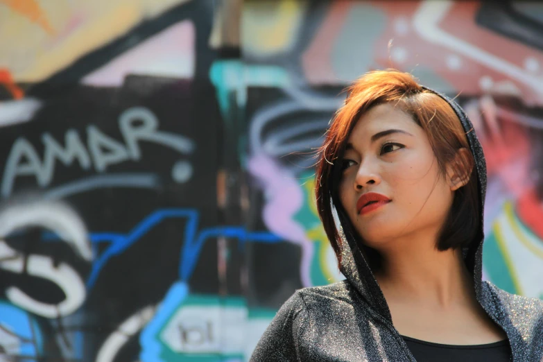 a woman standing in front of a graffiti covered wall, inspired by Bernardino Mei, pexels contest winner, wearing a hood with pointy ears, with a bob cut, beautiful young asian woman, grungy; colorful