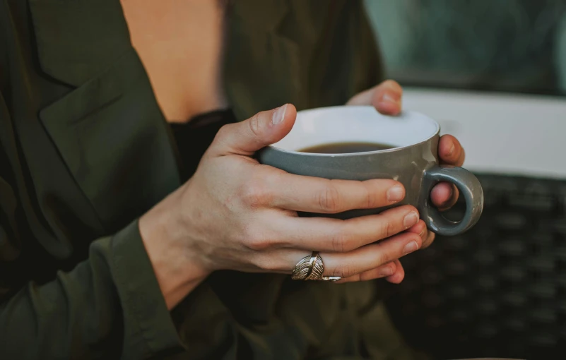 a close up of a person holding a cup of coffee, silver jewellery, wearing a dark dress, nordic wedding ring, afternoon hangout