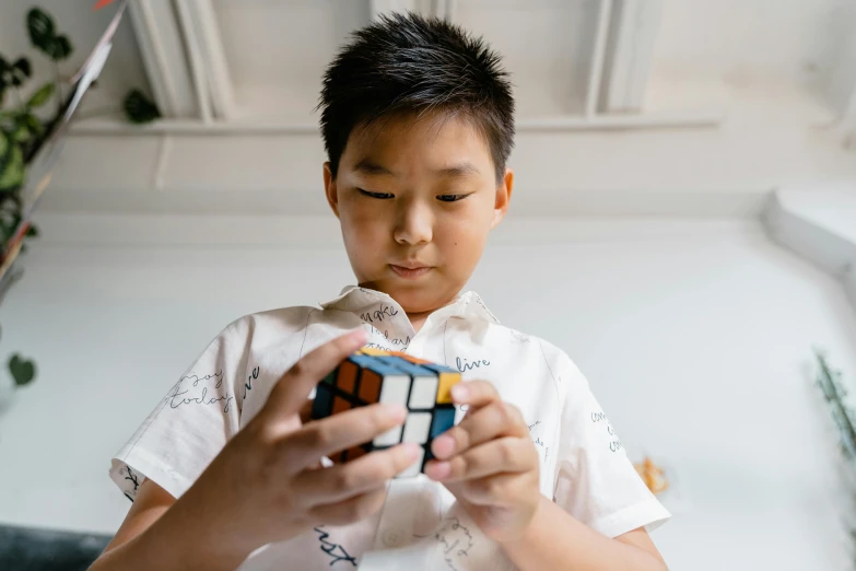 a young boy holding a rubik cube in his hands, inspired by Ernő Rubik, pexels contest winner, ross tan, looking partly to the left, louise zhang, screensaver