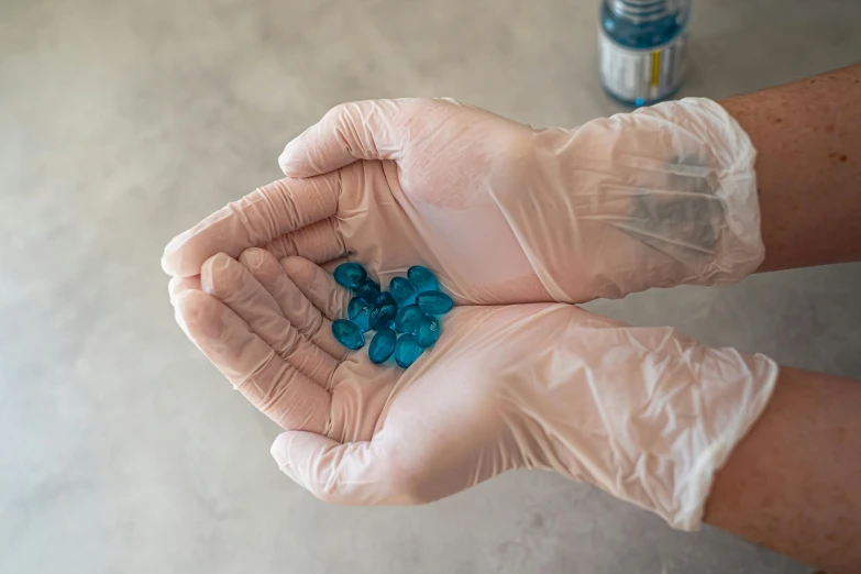 a person holding a handful of pills in their hands, by Ryan Pancoast, reddit, plasticien, blue gloves, hdpe, hands on counter, blue diamonds