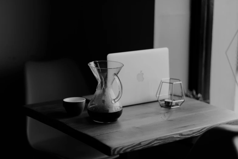 a laptop computer sitting on top of a wooden table, a black and white photo, by Romain brook, unsplash, klein bottle, wooden coffee table, cone shaped, set photo