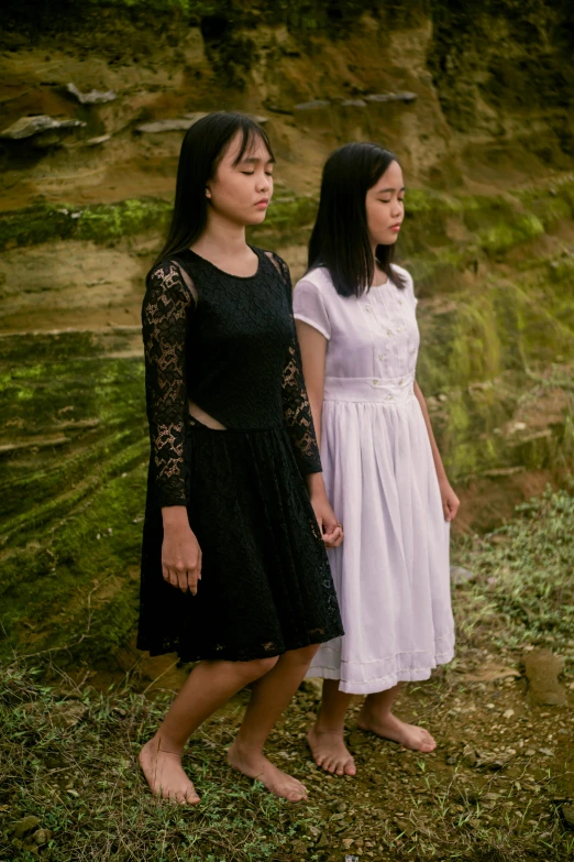 a couple of women standing next to each other, an album cover, inspired by Zheng Xie, unsplash, international gothic, standing on rocky ground, wearing dresses, ( ( ( ( kauai ) ) ) ), concert