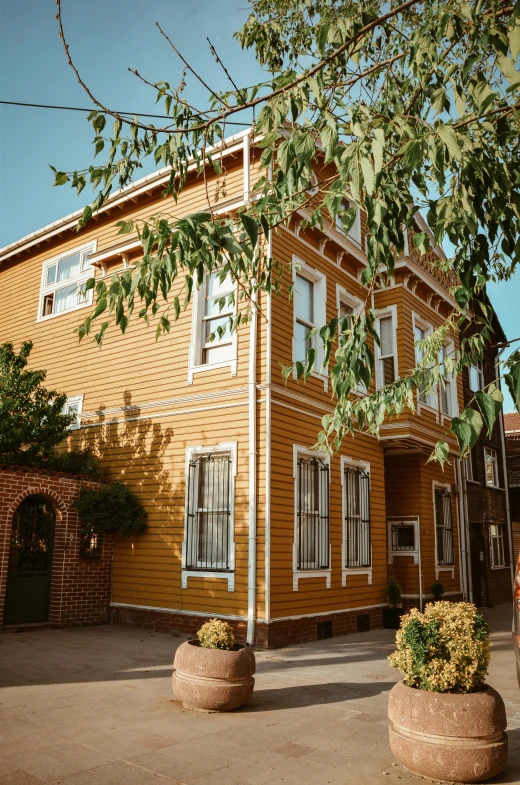 a yellow house with potted plants in front of it, a colorized photo, by Edward Avedisian, pexels, peaceful wooden mansion, street corner, profile image, golden colors