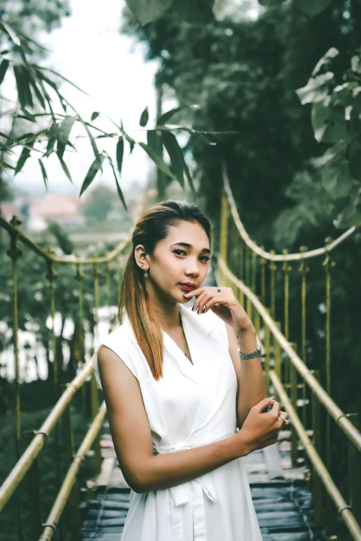a woman in a white dress standing on a bridge, inspired by Ruth Jên, pexels contest winner, south east asian with round face, greenery, handsome girl, malaysian