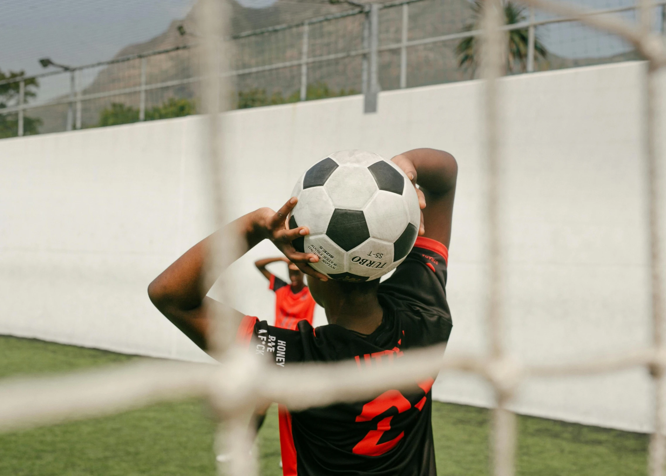 a young man holding a soccer ball over his head, pexels contest winner, happening, red mesh in the facede, black teenage boy, helmet view, 15081959 21121991 01012000 4k