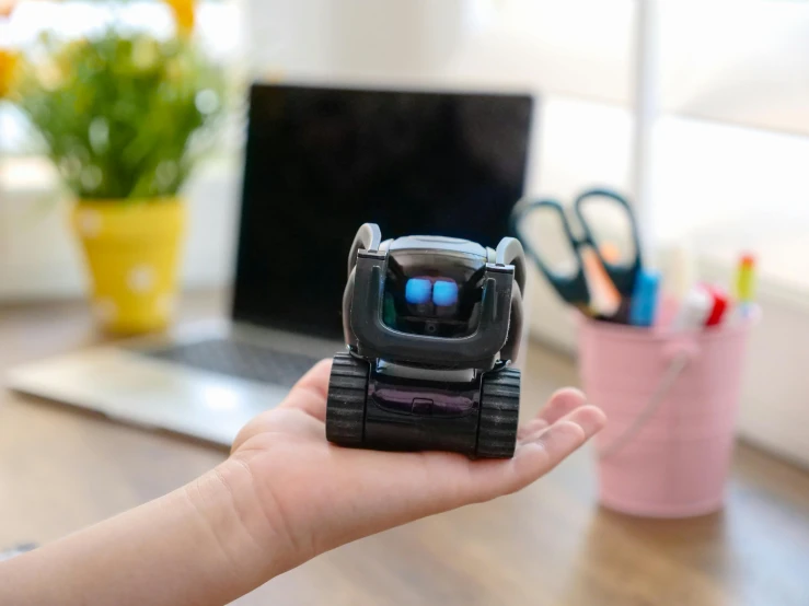 a person holding a toy robot in front of a laptop, by Julia Pishtar, unsplash, niko oneshot riding a roomba, very tiny, back of hand on the table, smol