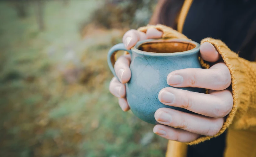 a person holding a cup of coffee in their hands, by Jessie Algie, trending on pexels, arts and crafts movement, forest picnic, turquoise rust, manuka, soft - warm