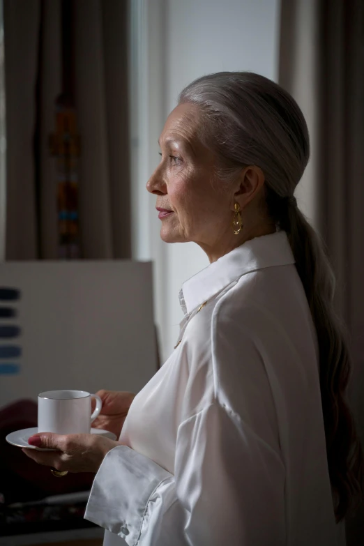 a woman in a white shirt holding a cup of coffee, a portrait, inspired by Grethe Jürgens, wearing silver hair, contemplative, hotel room, profile image