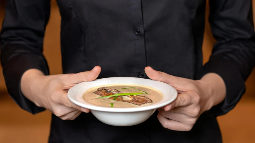 a woman in a black shirt holding a bowl of soup, inspired by Géza Dósa, gourmet michelin restaurant, beige, close-up photo, rectangle