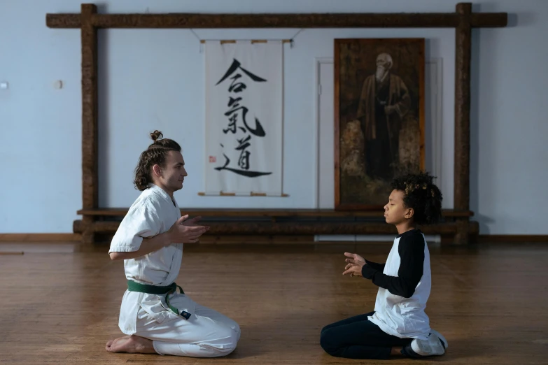 a couple of people sitting on top of a wooden floor, inspired by Baiōken Eishun, pexels contest winner, art & language, white belt, with a kid, teaching, kneeling