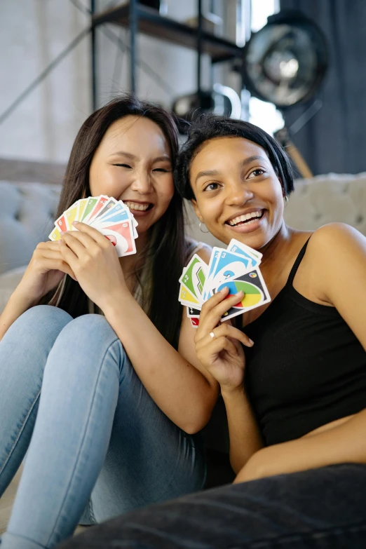 two women sitting on a couch holding playing cards, inspired by Aquirax Uno, happening, rainbow colored, teenager hangout spot, joy ang, vine