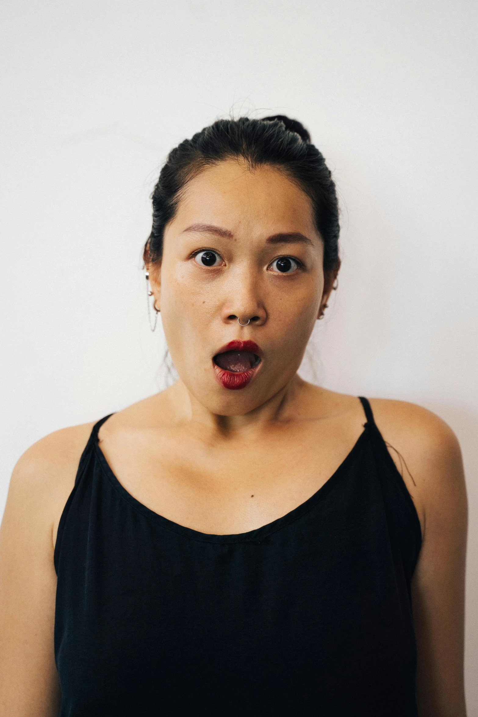 a woman with a surprised look on her face, inspired by Ruth Jên, pexels contest winner, mingei, she is wearing a black tank top, set against a white background, tongue sticking out, asian features